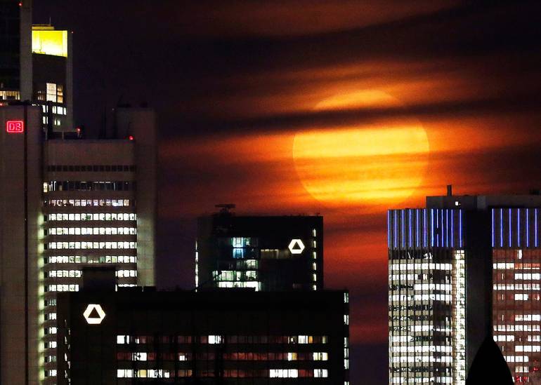 13.ซุปเปอร์มูนส่องแสงสีส้มลอดกลุ่มเมฆลงมาในเขตธนาคาร ในนครแฟรงก์เฟิร์ต ประเทศเยอรมนี